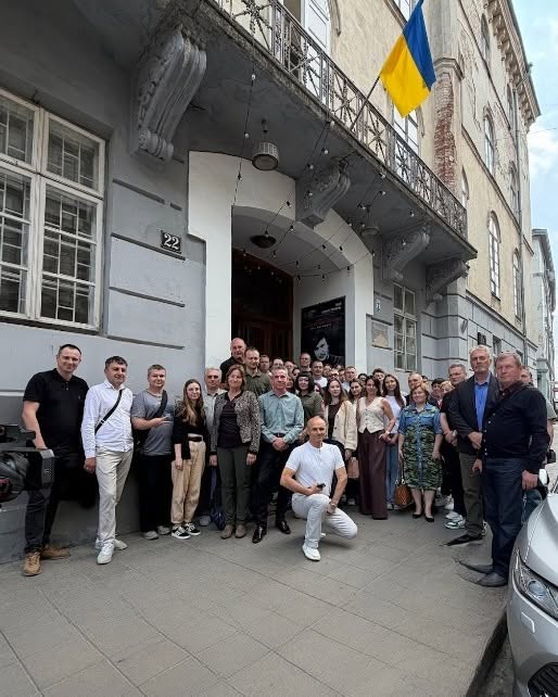 Ukraine Visit Group Photo Group photo outside a building in Lviv, Ukraine with a Ukrainian flag above the entrance.